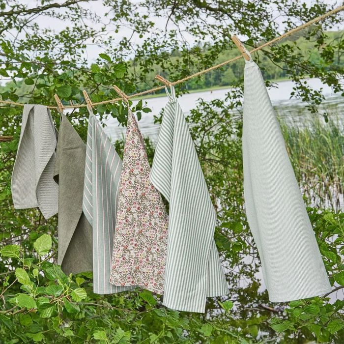 Forskellige køkkentekstiler i blå/grønne nuancer hænger til tørre på snor udendørs