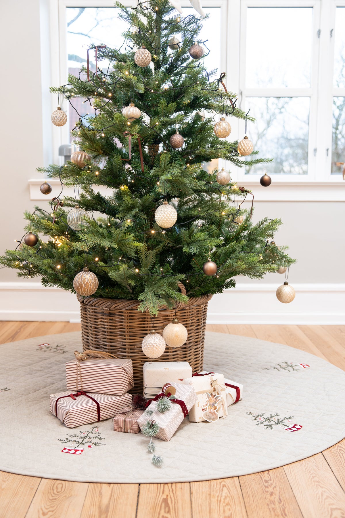 Christmas tree with ornaments in a basket, standing on a quilted, embroidered tree skirt