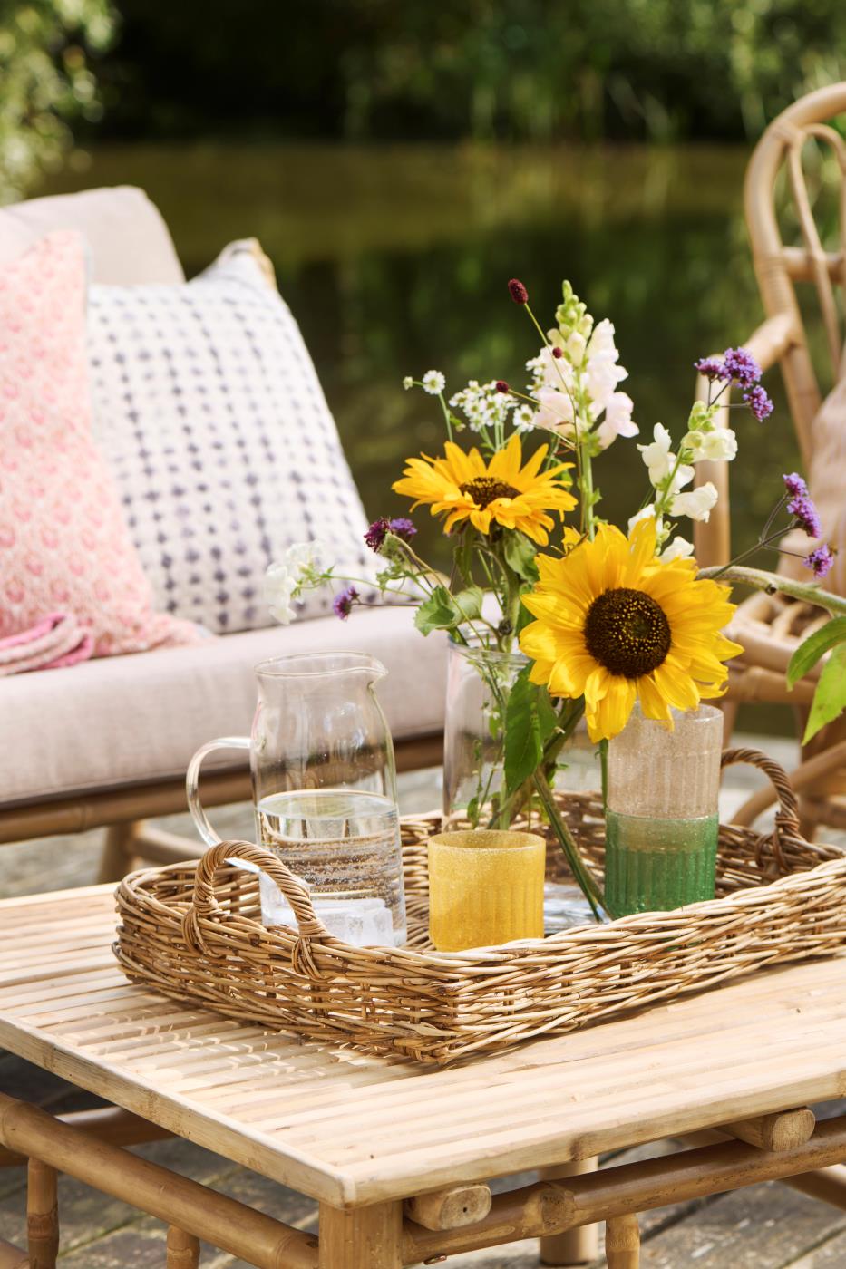 Cylinderglasvase med solsikker i på bakke på havesofabord.