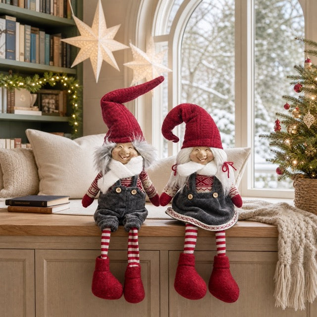 Christmas gnome trolls in red and gray clothing with dangling legs sitting on a ledge