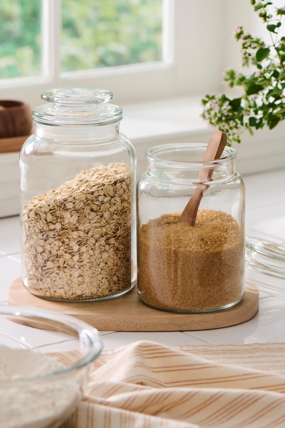 Glass storage jar with dry goods and a wooden spoon on a bright kitchen table by the window