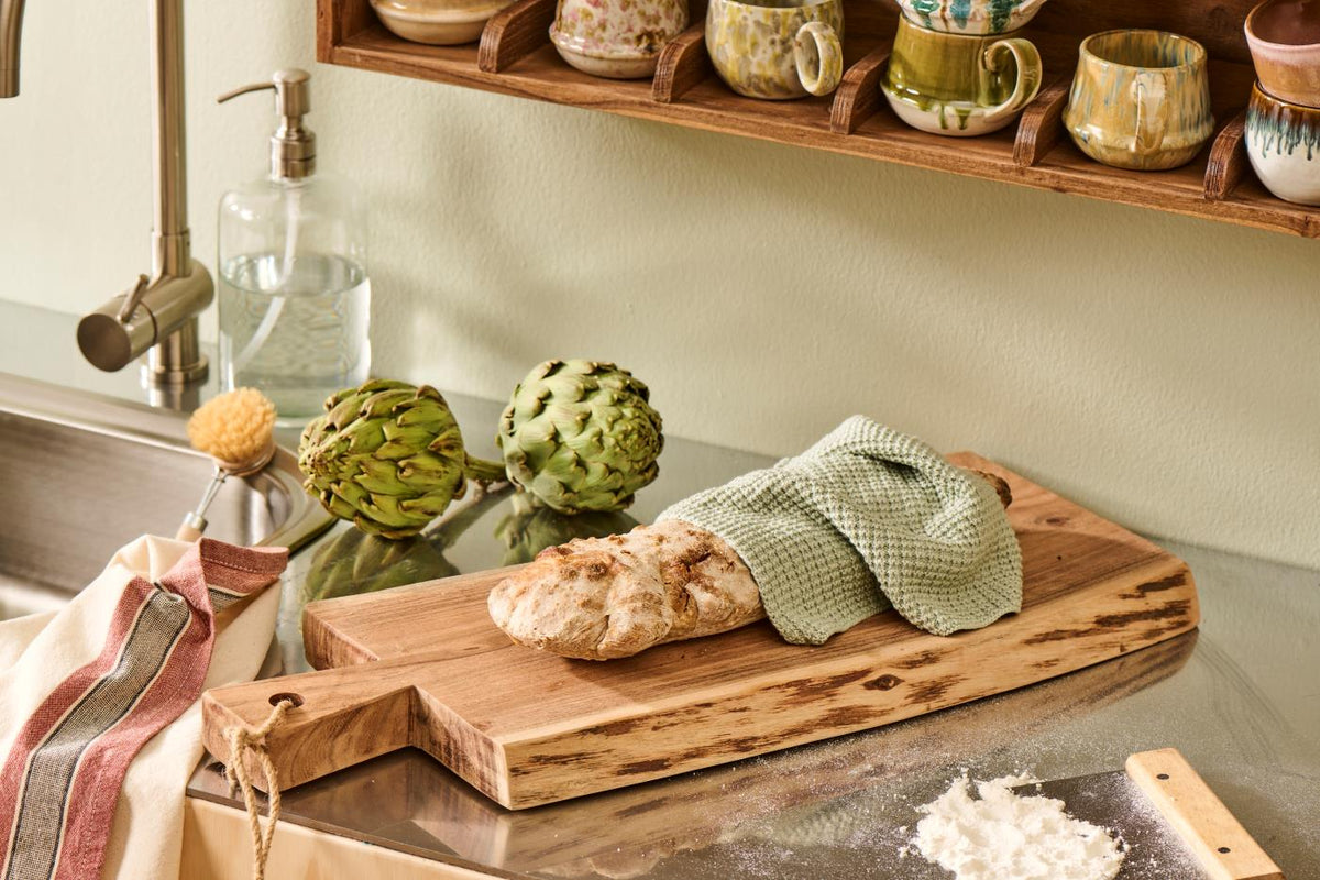 Dusty green knitted dishcloth from the Mynte-serien on a kitchen table with bread and kitchen accessories