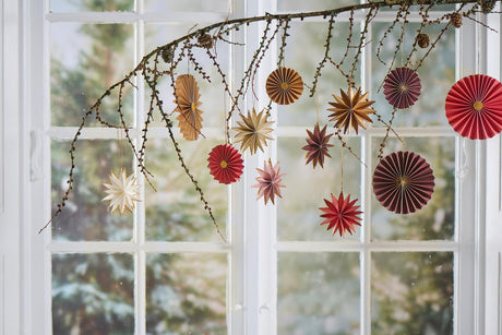 Larch branch hanging in front of a window decorated with paper ornaments from Ib Laursen