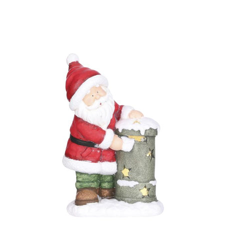 Julemanden iført rødt og hvidt juletøj, grønne bukser og brune støvler, står ved en sneklædt postkasse med stjerner, der lyser.