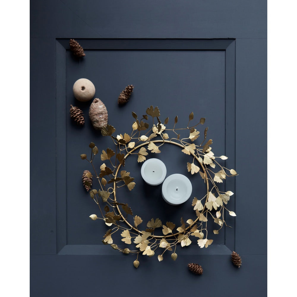 Blue door laid flat with a gold-colored wreath with leaves from House Doctor, arranged with pine cones and pillar candles