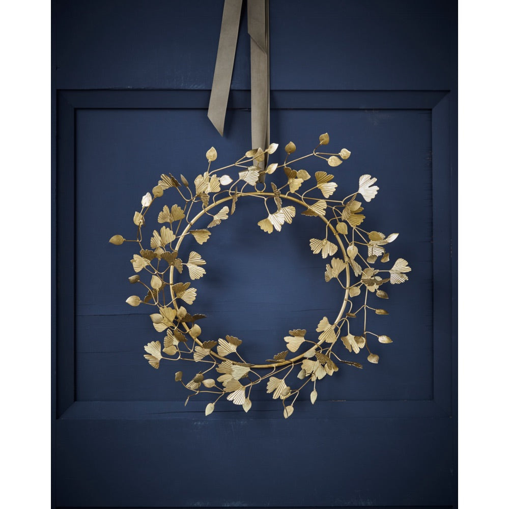 Wreath with gold-colored leaves from House Doctor hung by a ribbon on a blue door