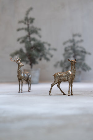 Polyresin deer with gold finish standing in front of trees