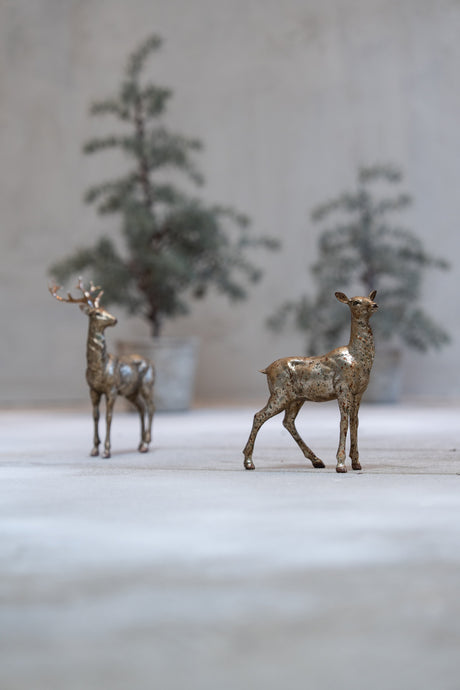 Polyresin deer with gold finish standing in front of trees