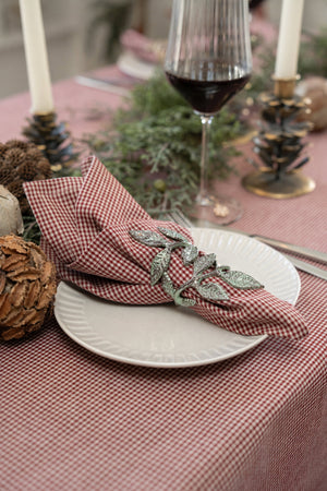 Antique green napkin ring with small leaves surrounding a red-and-white checked cloth napkin on a festively set Christmas table