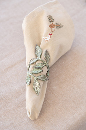 Antique green napkin ring with a leaf motif around a light fabric napkin with a Christmas motif, on a plate over a linen-colored tablecloth