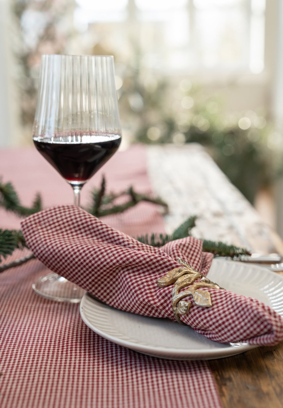 Antique gold-tone napkin ring with small leaves around a checked fabric napkin on a set table