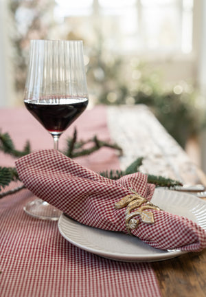 Antique gold-tone napkin ring with small leaves around a checked fabric napkin on a set table
