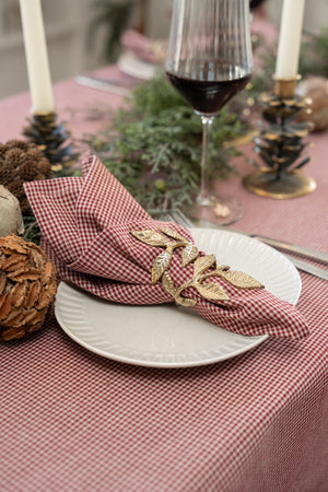 Antique gold-tone napkin ring with a leaf motif around a light fabric napkin on a plate with a pink tablecloth and rustic table decor
