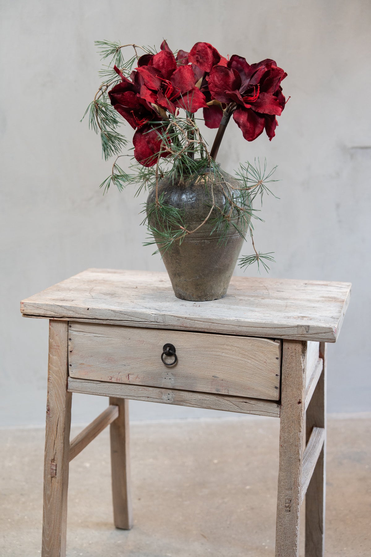 Bouquet of artificial amaryllis stems with burgundy flowers and pine branches in a vase
