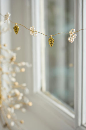Garland with white beads and gold-tone leaves from Ib Laursen, hanging as a window decoration
