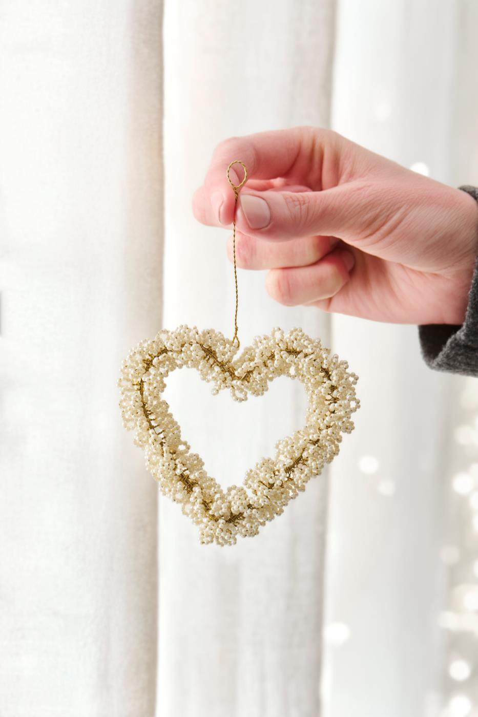 Hand holding a hanging heart with white beads by Ib Laursen