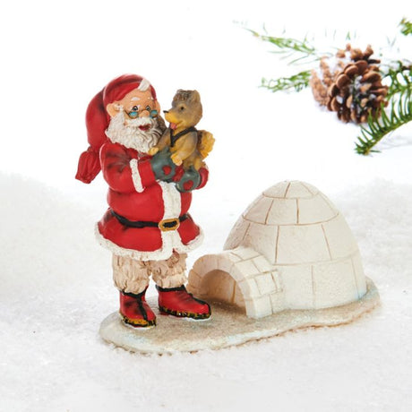 Julemand står på en isflage med iglo. Han bærer en slædehundehvalp i armene. Julemanden ser klog og glad ud, fra Pobra. 