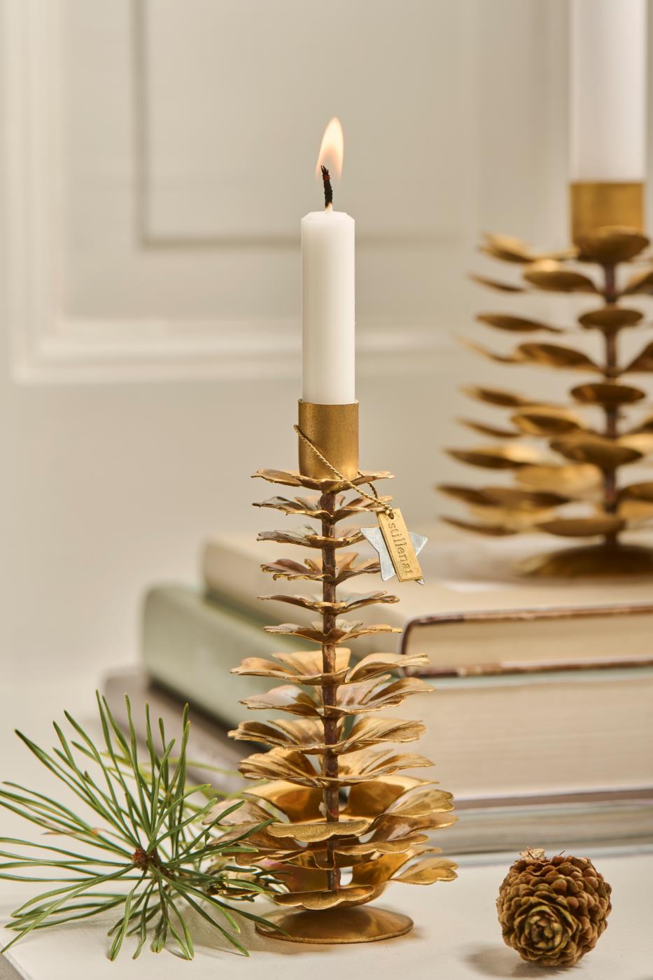 Brass pinecone candle holder with white taper candle, accented with a pine sprig and pinecone