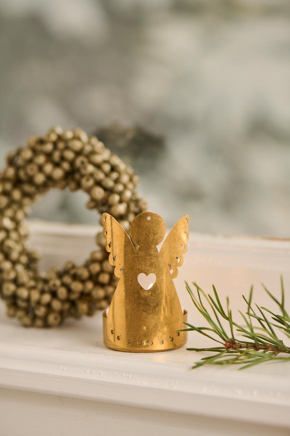 Gold-colored angel tealight candle holder from Ib Laursens Gloria series, standing on a windowsill with a wreath