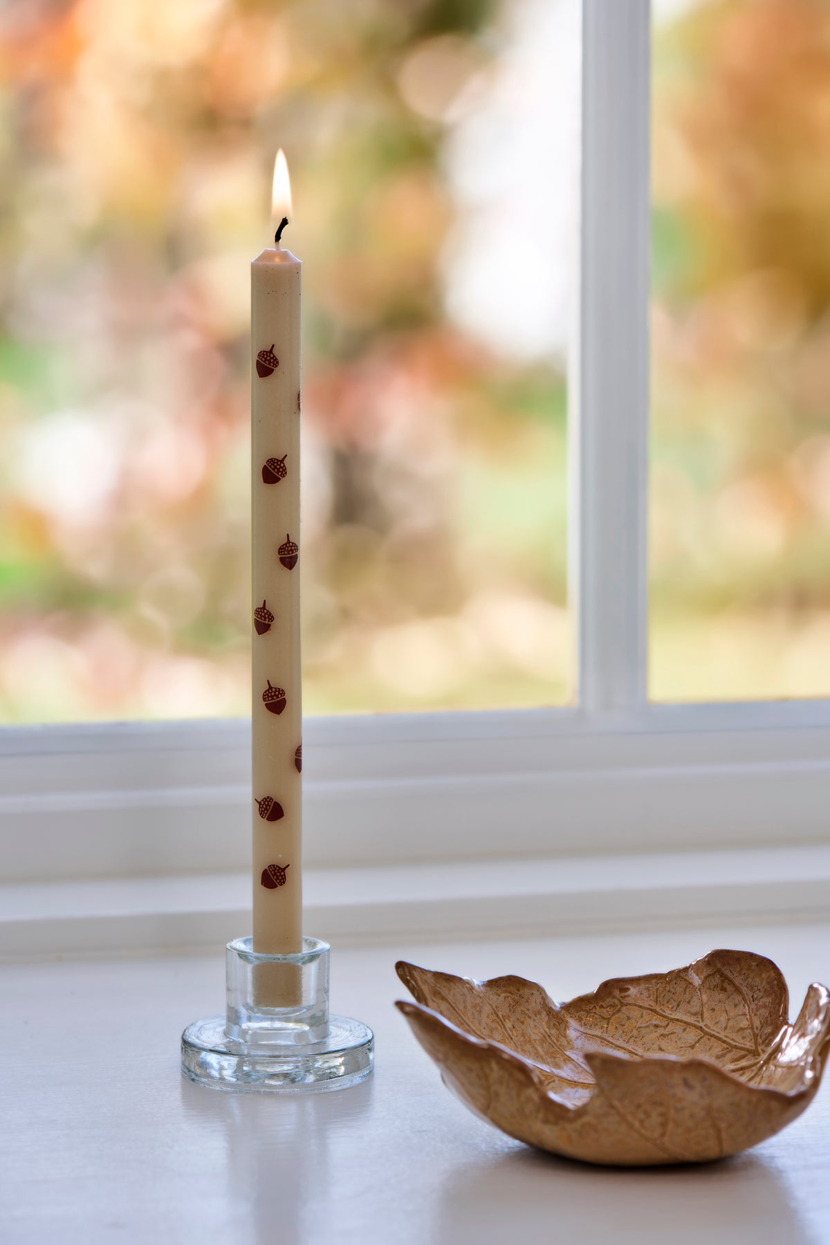 Candle with an acorn in a glass candle holder with a leaf-shaped dish beside