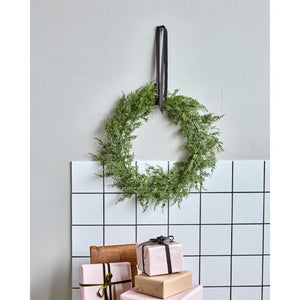 Wreath of artificial thuja branches from House Doctor hanging on the wall with a wide velour ribbon