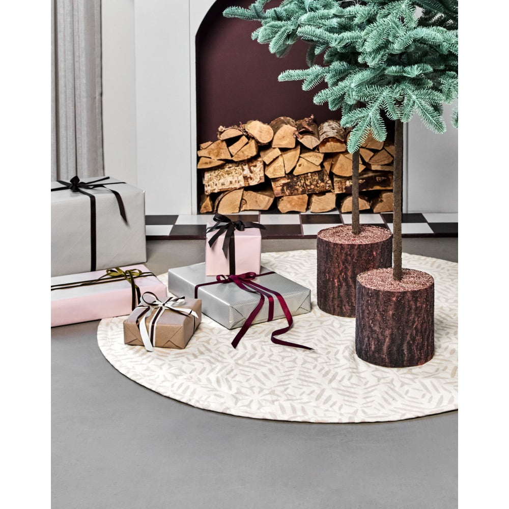 House Doctor Christmas tree skirt sits beneath two single-stem trees, with presents underneath and a fireplace in the background