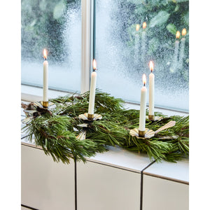 Clip-on candle holder with white taper candles attached to an artificial fir on a windowsill