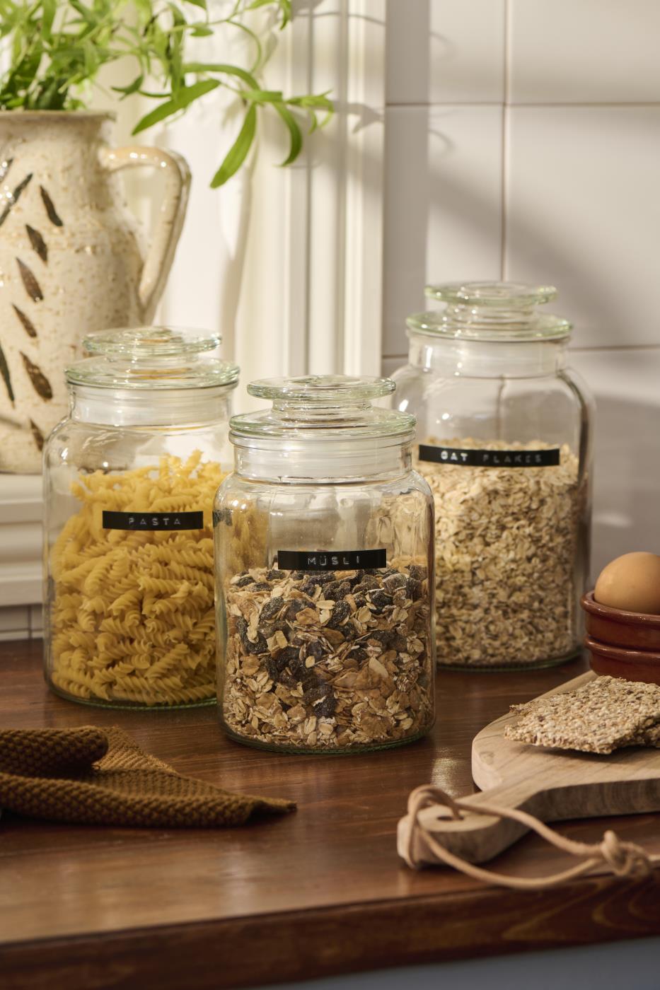 Three storage jars in varying sizes filled with dry goods on a countertop in a bright kitchen