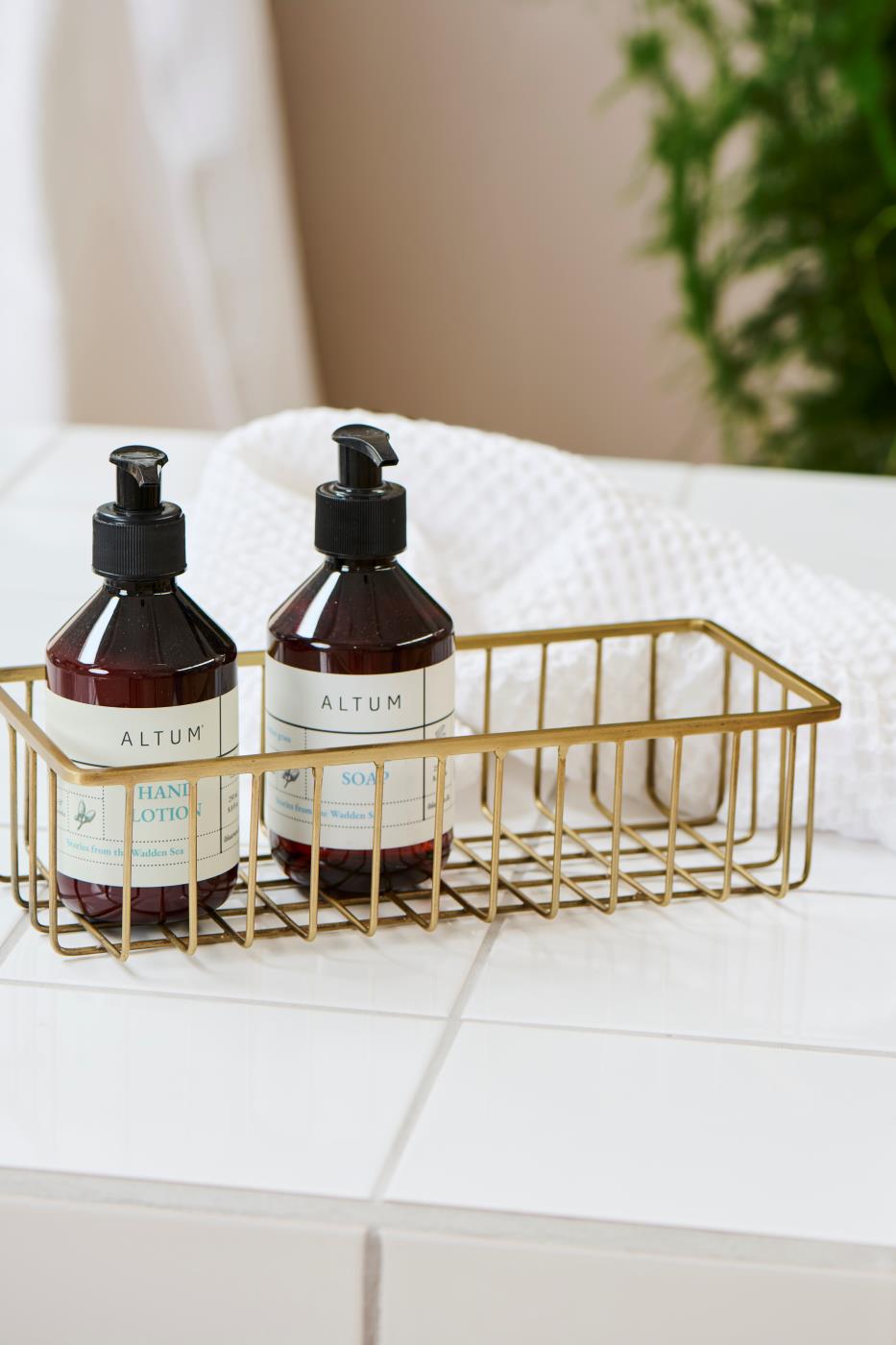 Two brown ALTUM pump bottles from Ib Laursen in a decorative gold-colored wire basket