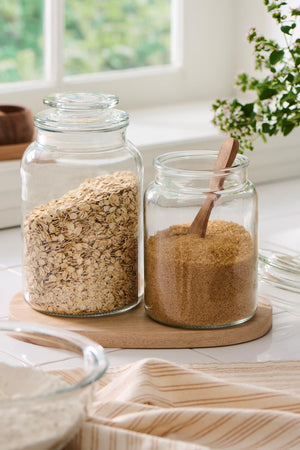 Glass storage jar with dry goods and a wooden spoon on a bright kitchen table by the window