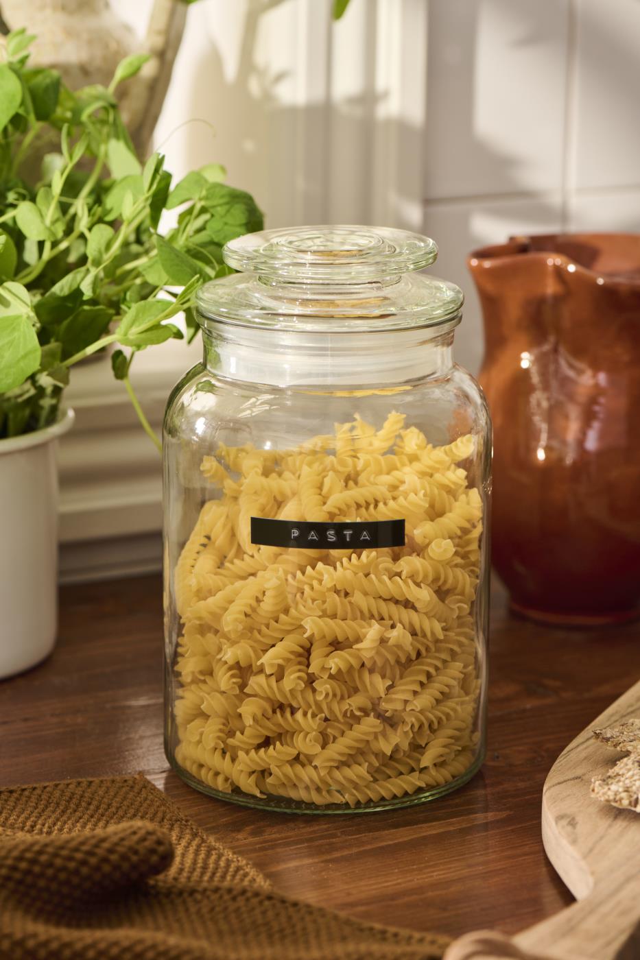 Glass storage jar with lid filled with pasta on a rustic kitchen table