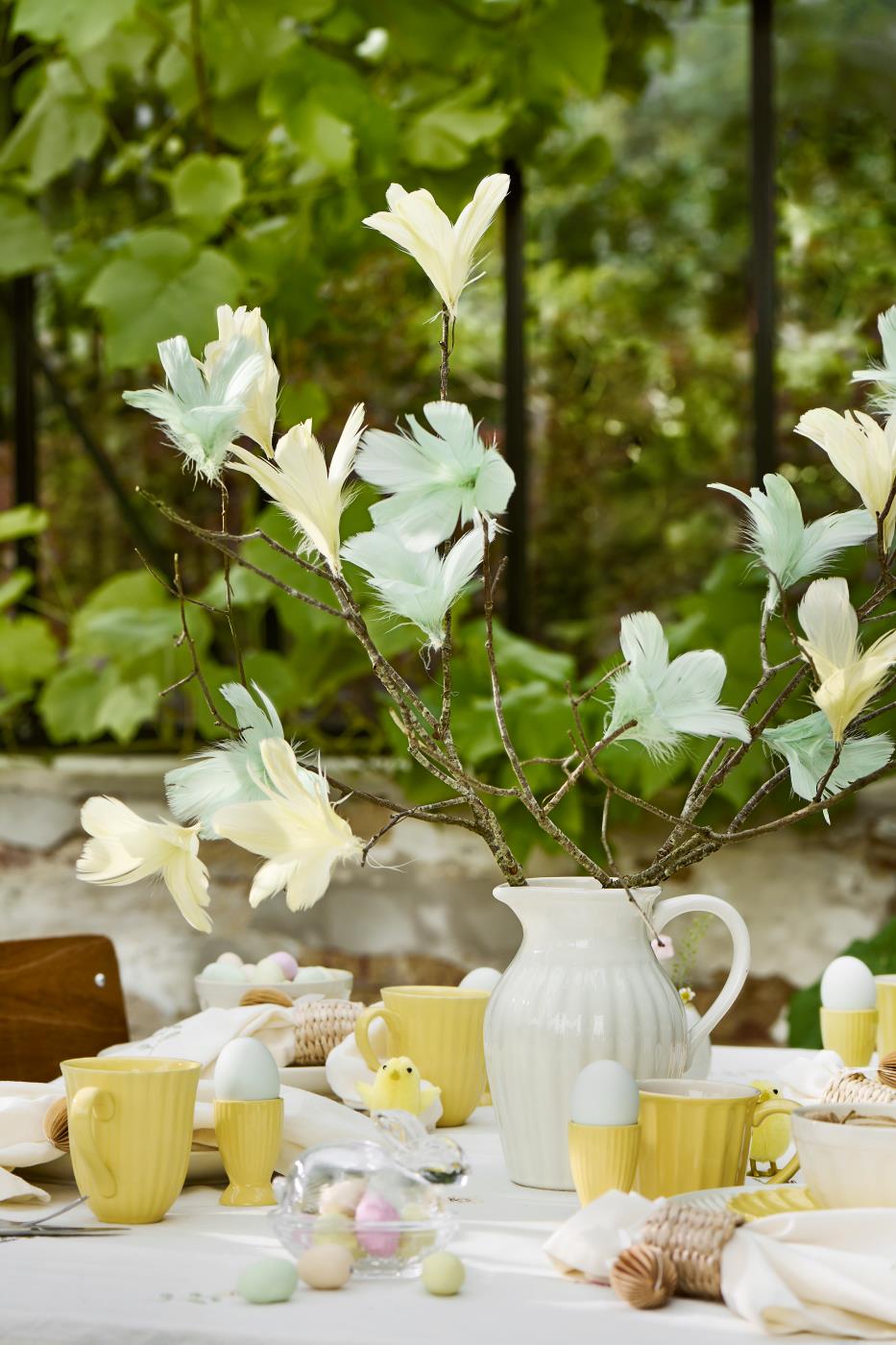 Kande på bord med grene pyntet med pyntefjer