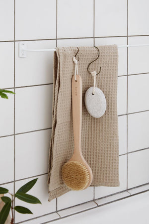 Beige Liseleje towel and washcloth hanging on a wooden rod in a bathroom with white tiles
