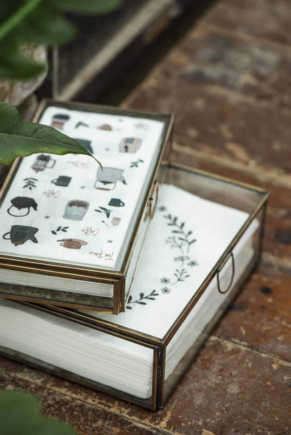 Glass display box with an antique gold frame and patterned napkins on a rustic wooden table