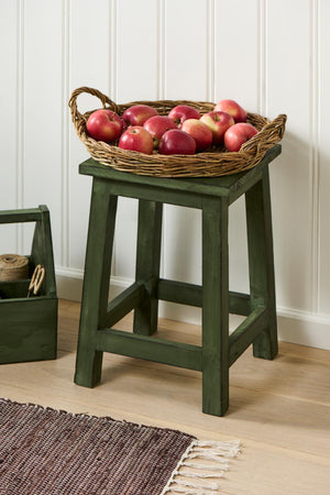 Round willow-woven tray with red apples on a green wooden stool