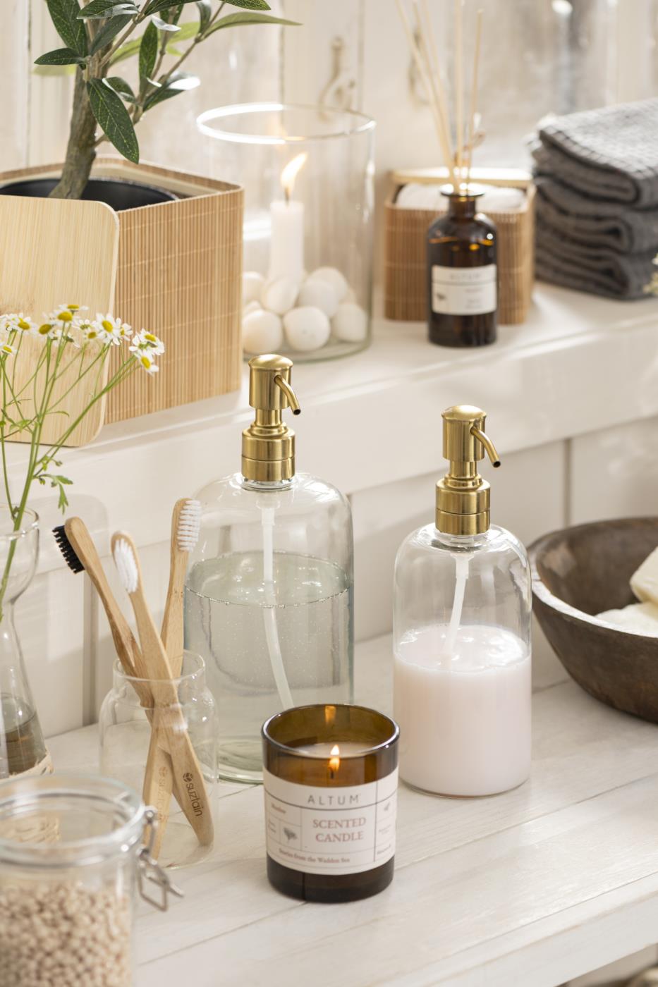 Clear glass soap dispenser with brass-colored pump, hand cream and soap in the bathroom