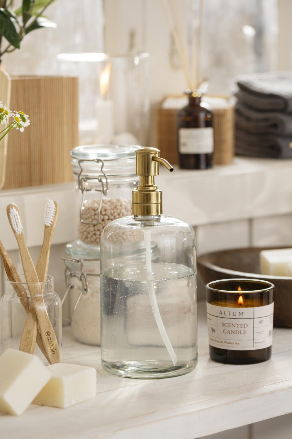 Soap dispenser with brass-colored pump from Ib Laursen on a bathroom vanity with personal care products