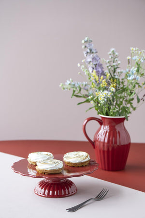Red Mynte vase from Ib Laursen with flowers on a set table alongside a red footed cake stand with small cakes