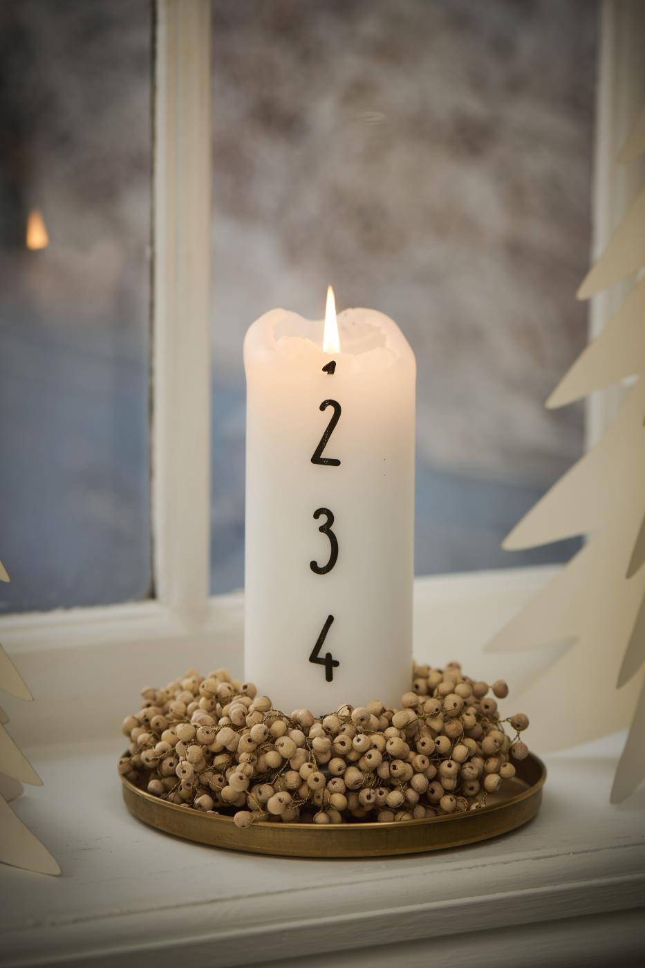 Numbered advent candle on a brass tray decorated with a small wooden bead garland