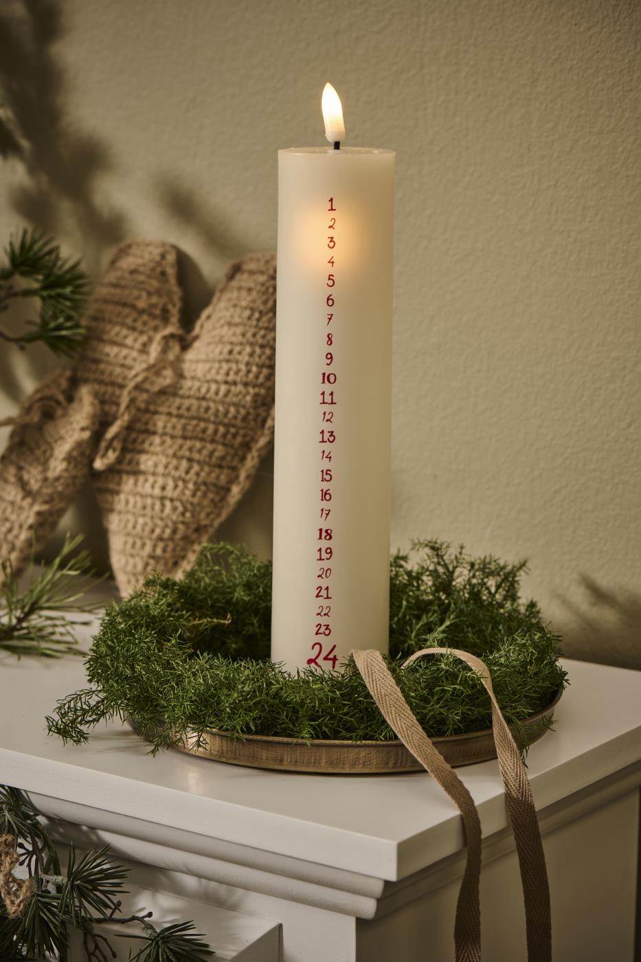 Brass tray with a tall advent candle and green fir sprigs in a cozy Christmas display