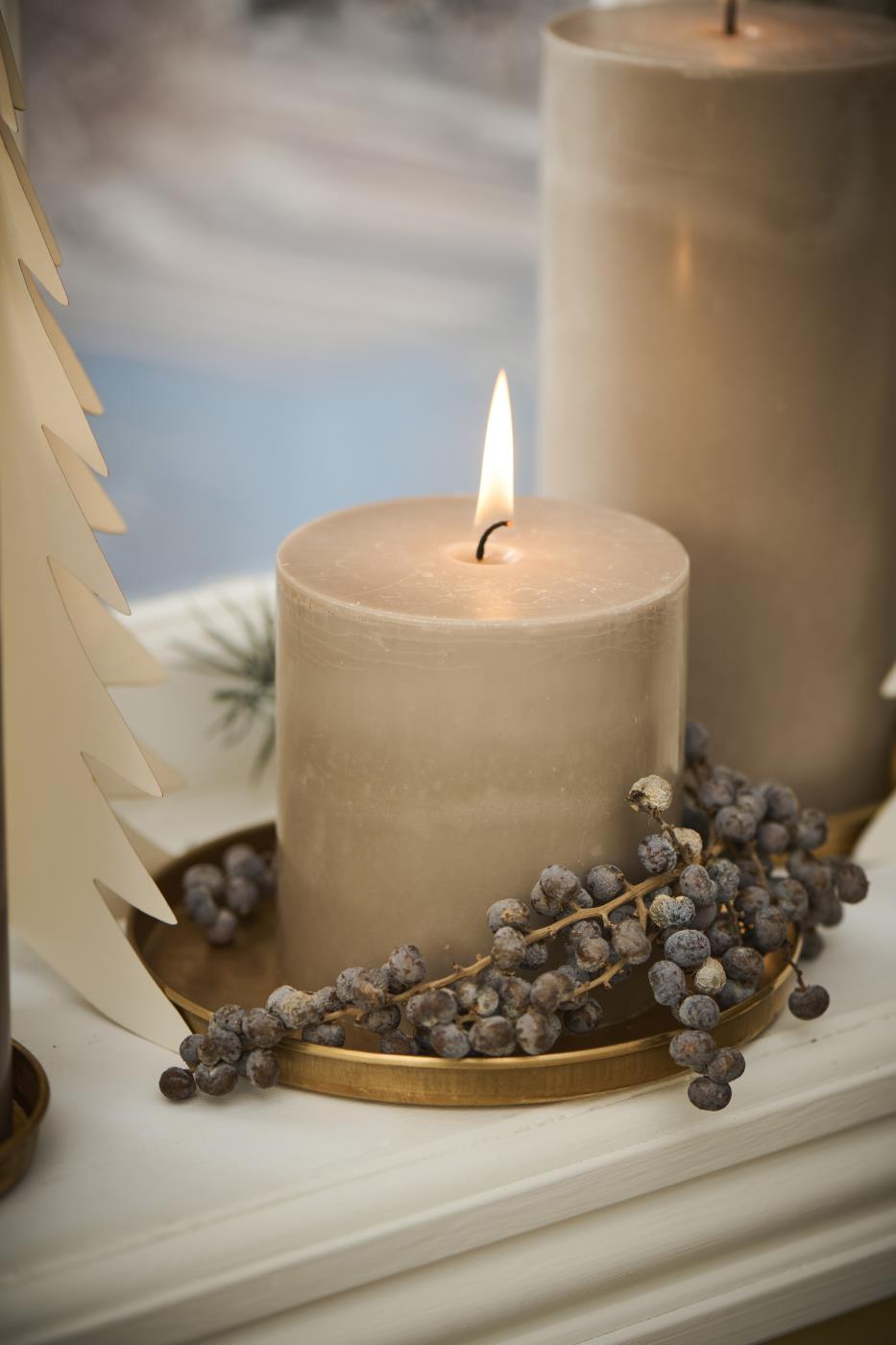 Pillar candle on a round brass tray with decorative branches and natural ornaments on the windowsill