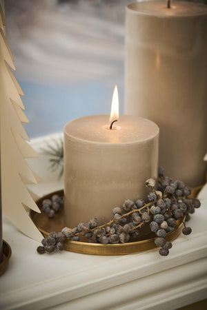 Pillar candle on a round brass tray with decorative branches and natural ornaments on the windowsill