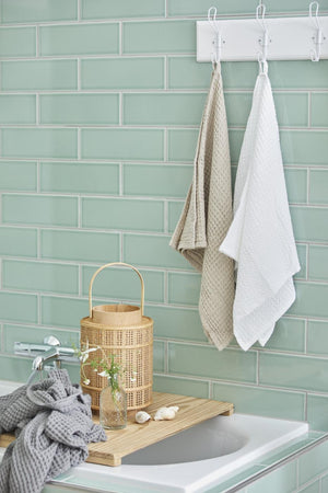 White Liseleje towels with a waffle weave hanging by the sink in a bathroom with green tiles