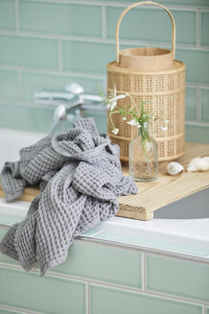 Anthracite-gray Liseleje towel with waffle texture beside a bathtub with green tiles