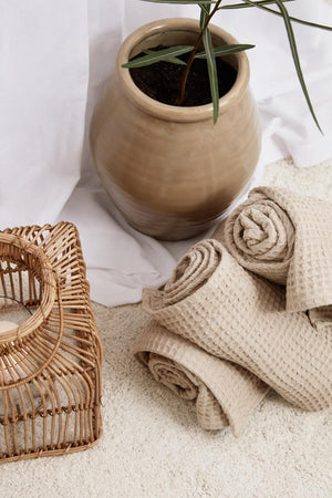 Folded beige Liseleje towels beside a small plant and a basket in natural materials